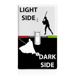 May include: A light switch cover with a Star Wars theme. The top half is white with the text "LIGHT SIDE" and a silhouette of Luke Skywalker holding a lightsaber. The bottom half is black with the text "DARK SIDE" and a silhouette of Darth Vader holding a lightsaber. The switch is in the middle and says "OFF".