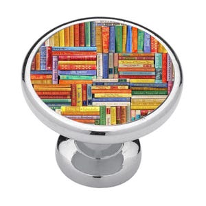 May include: A round, silver-toned metal cabinet knob featuring a flat, circular face decorated with a colourful, dense collage of miniature book spines. The books display various titles and text, including Let It Sew, Oh Darn, and Diary of a Fabricholic.