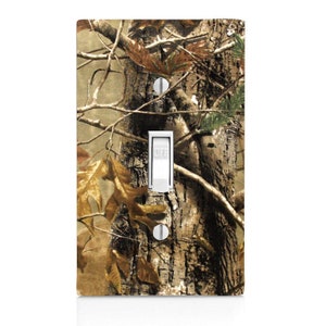 May include: A light switch cover with a camouflage pattern featuring brown, green, and tan colors. The switch cover has a white toggle switch with the word "OFF" printed on it.