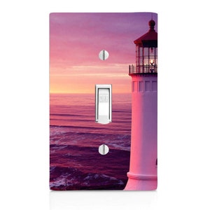 May include: A light switch cover featuring a photograph of a white lighthouse with a red roof against a pink and purple sunset over the ocean.
