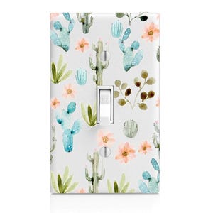 May include: A light switch cover with a watercolor design featuring cacti, flowers, and leaves in shades of green, blue, and pink. The switch cover is white and has the word "OFF" printed on it.