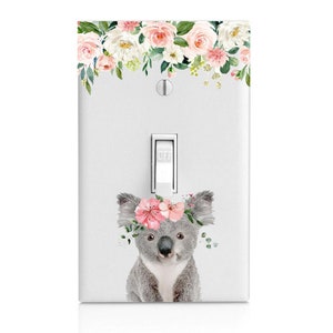 May include: A light switch cover with a floral design at the top and a koala wearing a pink flower crown in the bottom half. The switch is labeled "OFF".