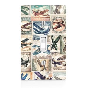 May include: A decorative light switch cover featuring a collage of vintage airplane illustrations in shades of blue, brown, and green. The switch itself is white, with the word "OFF" visible. The design evokes a retro aviation theme.
