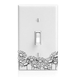 May include: White light switch cover with a black and white daisy floral design. The switch is in the "off" position. The cover has two screws and a rectangular switch.