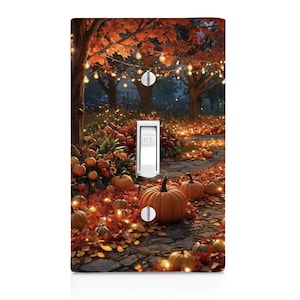 May include: A decorative light switch cover featuring a fall scene with pumpkins, fallen leaves, and trees with orange foliage. The switch is in the "OFF" position. The background includes a pathway and string lights.