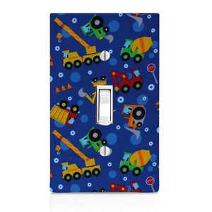 May include: A blue light switch cover with a pattern of construction vehicles, including a crane, a cement mixer, a dump truck, and a backhoe. The switch cover has a white light switch with the words "OFF" printed on it. The pattern also includes blue circles and white bolts.