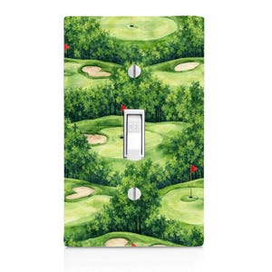May include: A rectangular light switch cover plate featuring a repeating watercolor pattern of a golf course with green fairways, sand bunkers, and red flags. The white toggle switch in the center has the word OFF printed on it in black text.