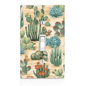 May include: A light switch cover with a cactus and succulent pattern. The cover features a variety of cacti and succulents in shades of green, blue, and orange on a light brown background.