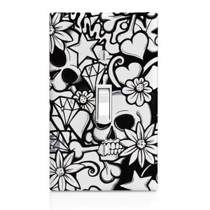 May include: Black and white light switch cover with a skull, hearts, stars, and flowers. The design is a graphic pattern.