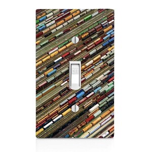 May include: A decorative light switch cover featuring a colorful aerial view of a train yard. The image includes a variety of train cars in shades of red, yellow, blue, and green. The switch itself is white with the word "OFF" printed on it.