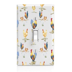 May include: White light switch cover with a repeating watercolor pattern of roosters and hens in shades of blue, yellow, and red. The switch is in the "off" position. The design has a farmhouse or country theme.