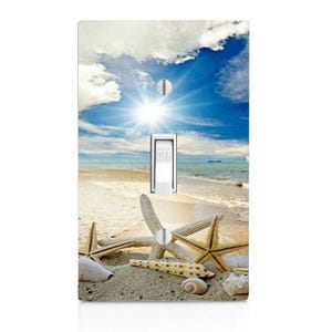 May include: A light switch cover with a beach scene featuring a blue sky, white clouds, a bright sun, and starfish on a sandy beach.