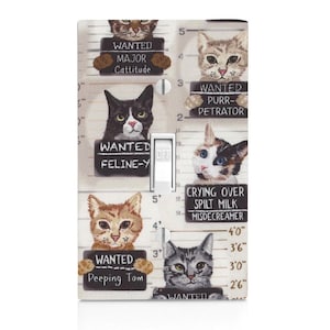 May include: A light switch cover with a white background and a black and white illustration of cats with wanted posters. The posters have text that says "Wanted Major Cattitude", "Wanted Feline-Y", "Wanted Purr-petrator", "Crying Over Spilt Milk Misdecream", and "Wanted Peeping Tom".