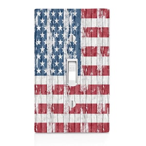 May include: A light switch cover with a distressed American flag design on a white wood background. The switch is labeled "OFF".