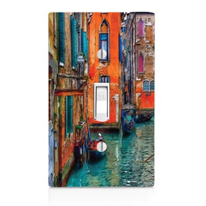 May include: A light switch cover featuring a colorful painting of a canal in Venice, Italy. The painting depicts buildings with orange, red, and blue accents, and a gondola on the water. The switch is labeled "OFF".