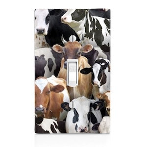 May include: A decorative light switch cover featuring a collage of cow faces in various colors and patterns. The switch is white with an "OFF" indicator. The background is a mix of black, white, and brown cows.
