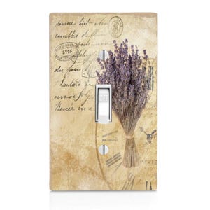 May include: A light switch cover with a vintage design featuring a bouquet of lavender, a clock face, and handwritten text in French. The text reads "toujours prêt à vous recevoir" which translates to "always ready to receive you".