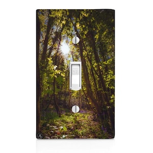 May include: A light switch cover with a photograph of a sunlit forest path. The path is lined with trees and green foliage. The switch is labeled "OFF".