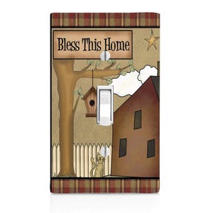 May include: A light switch cover with a brown house, a tree with a birdhouse, a cat, and a sign that says "Bless This Home". The background is a red and brown plaid pattern.