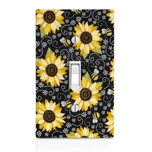 May include: A black light switch cover with a pattern of yellow sunflowers, white flowers, and yellow bees on a black background. The switch is labeled "OFF".