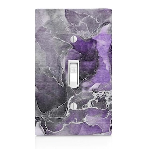 May include: A single-gang light switch cover with a marbled design in shades of purple, gray, and white. The switch is in the "off" position. The cover is rectangular with two screw holes and a white toggle switch.