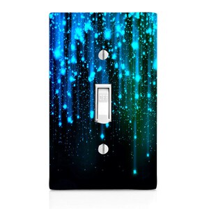 May include: A light switch cover with a blue and green abstract design. The design features streaks of light and small dots against a dark background. The switch is white and in the "OFF" position.