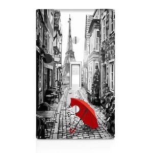 May include: A black and white illustration of a Parisian street with the Eiffel Tower in the background. A red umbrella lies on the cobblestone street.