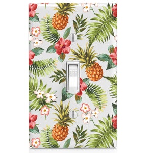 May include: A light switch cover with a tropical print featuring pineapples, hibiscus flowers, and palm leaves on a light gray background.