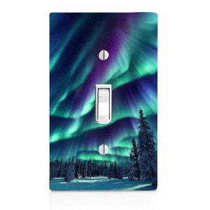 May include: A decorative light switch cover featuring a vibrant image of the aurora borealis. The design showcases a night sky with swirling green and purple lights above a snowy landscape with evergreen trees. The switch is in the "OFF" position.