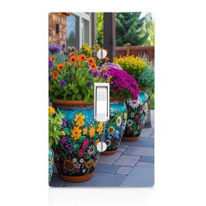 May include: A decorative light switch cover featuring a vibrant garden scene. The cover showcases a row of colorful flower pots filled with blooming flowers in shades of orange, yellow, purple, and pink. The switch is in the "OFF" position.