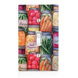 May include: A light switch cover with a watercolor design of jars filled with various vegetables, including beans, bell peppers, carrots, and green beans. The jars have handwritten labels that say "Beans", "Bell Peppers", and "Beans".