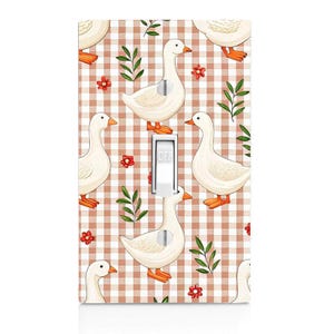 May include: A rectangular light switch cover plate featuring a repeating pattern of white geese with orange beaks and feet, interspersed with small red flowers and green leafy sprigs against a light brown and white checkered gingham background.