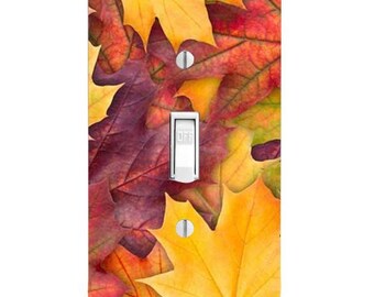 May include: A rectangular light switch cover plate featuring a vibrant autumn leaf pattern in shades of yellow, orange, red, and deep purple. The plate includes a central white toggle switch with the word OFF printed on it and two silver screws.