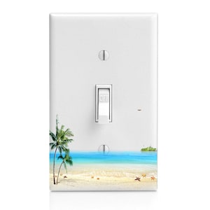 May include: White light switch cover with a beach scene. The design features a sandy beach, turquoise water, palm trees, and a small island. The switch is in the "OFF" position.