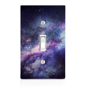 May include: A light switch cover with a galaxy design. The cover features a dark blue background with swirling clouds of purple, pink, and white. The switch is labeled "OFF".