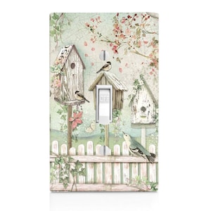 May include: A light switch cover with a vintage design featuring three birdhouses, a picket fence, and birds. The birdhouses are painted in shades of white, brown, and green. The fence is painted in shades of white and green. The birds are painted in shades of blue, brown, and white.