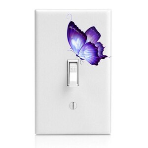 May include: A white light switch cover with a purple butterfly decal. The butterfly has a light blue center and is in flight.