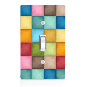 May include: A rectangular light switch cover plate featuring a grid of multicolored squares in shades of blue, pink, brown, yellow, red, and green. The plate has a central white toggle switch in the off position and two silver metal screws.