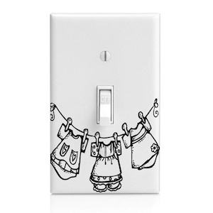 May include: A white light switch cover with a black and white illustration of three pieces of clothing hanging on a clothesline. The text "OFF" is on the light switch.