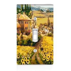 May include: A light switch cover featuring a painting of a quaint village nestled in a sunflower field. The scene depicts a winding path leading to a cluster of houses with red tile roofs, surrounded by lush greenery. The switch cover is a decorative way to add a touch of nature to any room.