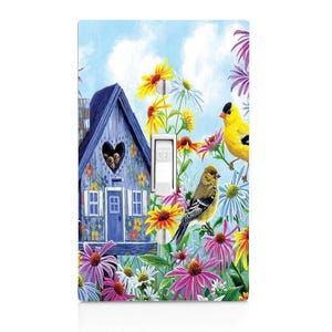 May include: A light switch cover with a colorful design featuring a blue birdhouse with a heart-shaped window, surrounded by flowers and two yellow birds. The switch is labeled "OFF".