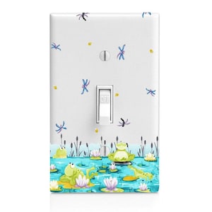 May include: A white light switch cover with a design of green frogs sitting on lily pads in a blue pond. There are also blue dragonflies and yellow fireflies on the cover. The switch is labeled "OFF".