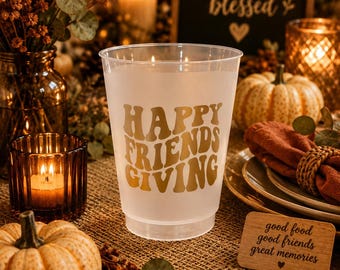 May include: A frosted plastic cup featuring the gold text "HAPPY FRIENDS GIVING" in a wavy font. The cup is translucent and cylindrical with a slightly tapered base, designed for holding beverages during seasonal gatherings and celebrations.