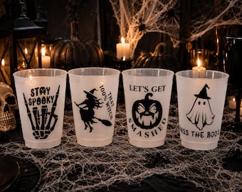 May include: Four translucent plastic cups featuring black Halloween-themed graphics and text. The designs include a skeleton hand with 'STAY SPOOKY', a witch on a broom with '100% THAT WITCH', a jack-o'-lantern with 'LET'S GET SMASHED', and a ghost with 'PASS THE BOO'S'.