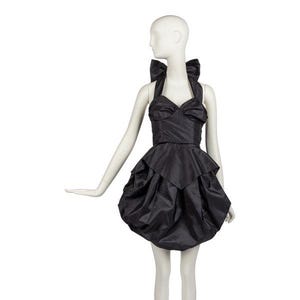 May include: A black, short dress with a halter neckline and a layered skirt. The dress features large bow details on the shoulders and bodice. The dress is displayed on a mannequin.