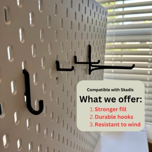 May include: A white pegboard with black hooks. The pegboard has evenly spaced holes and is designed to be compatible with Skadis. The text on the image says "What we offer: 1. Stronger fill 2. Durable hooks 3. Resistant to wind."
