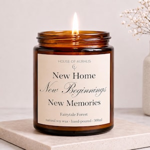 Könnte beinhalten: Eine brennende, bernsteinfarbene Glas-Kerze mit einem Etikett mit der Aufschrift "New Home, New Beginnings, New Memories". Die Kerze ist handgegossen mit natürlichem Sojawachs und hat ein Fassungsvermögen von 300 ml. Die Kerze steht auf einer steinfarbenen Oberfläche.