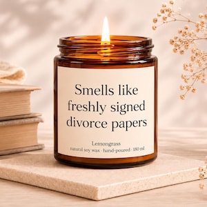 Könnte beinhalten: Eine brennende Kerze in einem bernsteinfarbenen Glas mit einem weißen Etikett, auf dem Smells like freshly signed divorce papers, Lemongrass, natural soy wax, hand-poured, 180 ml steht. Die Kerze hat eine Flamme und enthält natürliches Sojawachs.