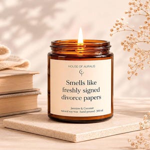 Könnte beinhalten: Eine brennende Kerze in einem braunen Glas mit einem Etikett mit der Aufschrift "Smells like freshly signed divorce papers". Die Kerze ist mit "Jasmine & Coconut, natural soy wax, hand-poured - 300 ml." beschriftet.