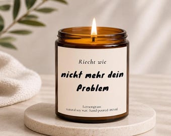 May include: A lit candle in an amber glass jar with a white label featuring the text Riecht wie nicht mehr dein Problem, Lemongrass, natural soy wax, hand-poured, 180 ml. The candle has a single burning wick and is filled with soy wax.